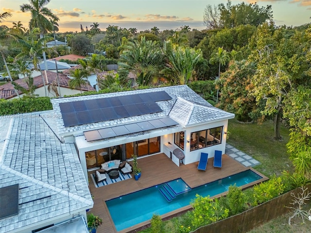 back house at dusk with an outdoor living space, a wooden deck, and solar panels