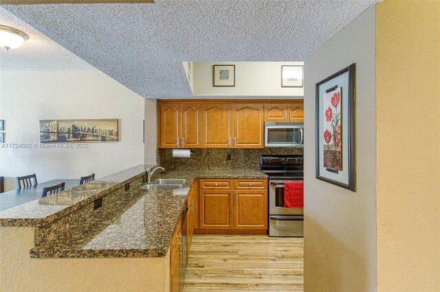 kitchen featuring appliances with stainless steel finishes, dark stone countertops, decorative backsplash, sink, and kitchen peninsula