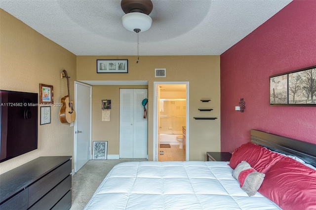 bedroom with a textured ceiling, ensuite bath, a closet, carpet flooring, and ceiling fan