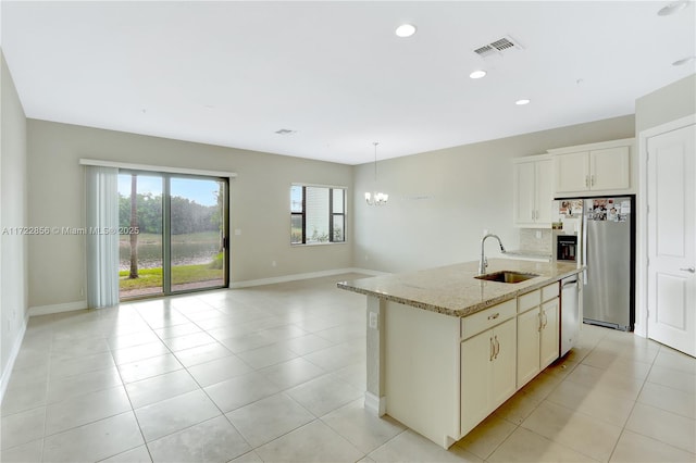 kitchen featuring a center island with sink, appliances with stainless steel finishes, light stone countertops, decorative light fixtures, and sink