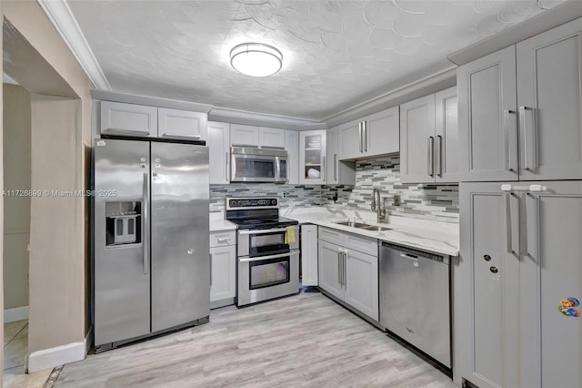 kitchen featuring stainless steel appliances, tasteful backsplash, light stone countertops, crown molding, and sink