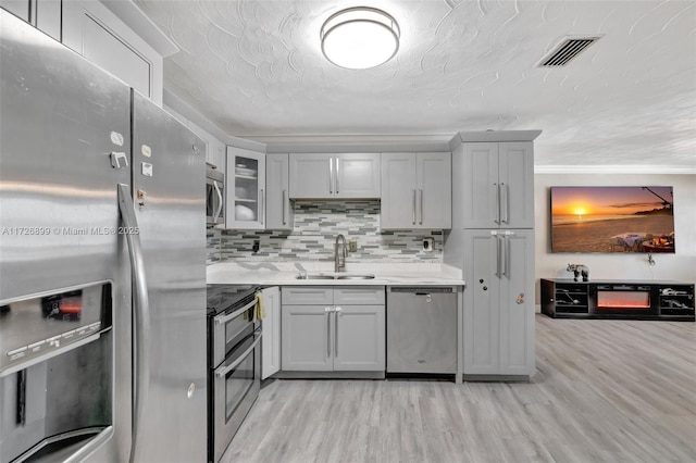 kitchen featuring appliances with stainless steel finishes, light hardwood / wood-style floors, sink, backsplash, and crown molding