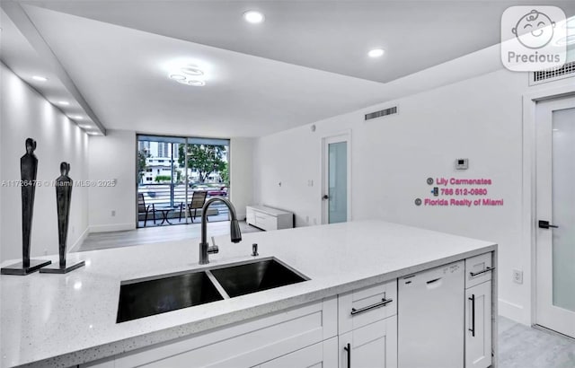 kitchen featuring sink, white cabinetry, light hardwood / wood-style flooring, white dishwasher, and light stone countertops