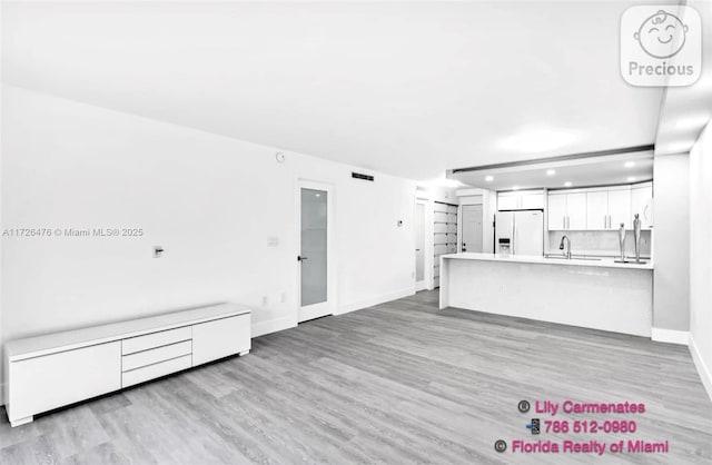 unfurnished living room featuring sink and light hardwood / wood-style flooring