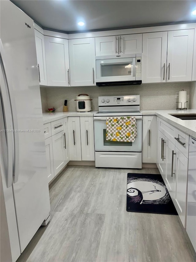 3725 NE 169th St Unit B-203, North Miami Beach, FL 33160 - kitchen with white cabinetry, light countertops, tasteful backsplash, white appliances, and light wood-style floors
