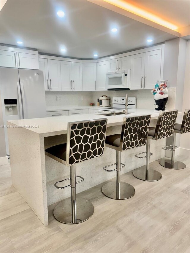 kitchen featuring white cabinetry, backsplash, white appliances, and a kitchen bar