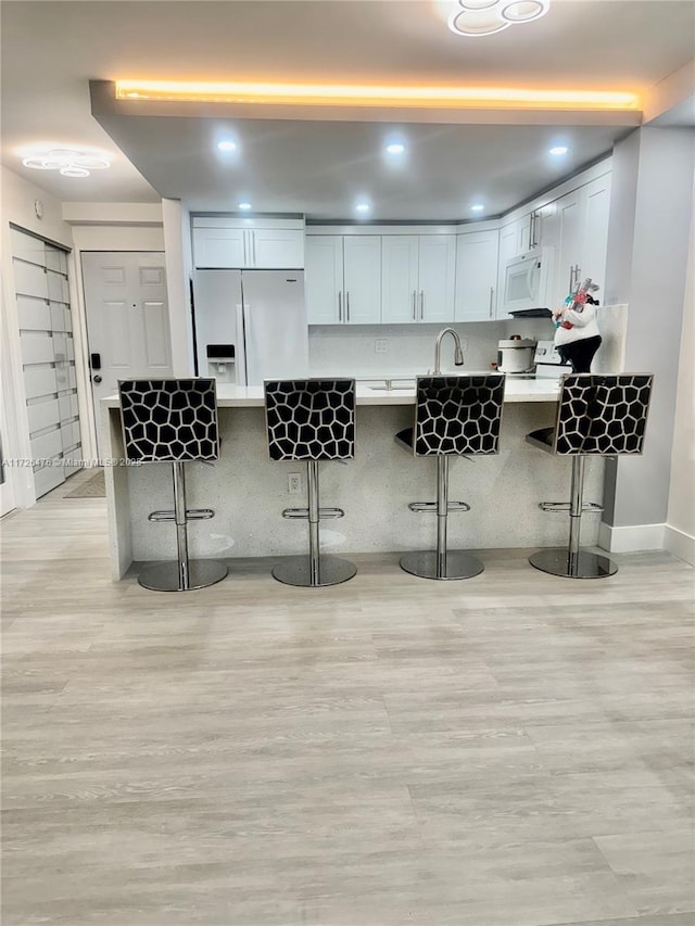 kitchen featuring white cabinetry, white appliances, a breakfast bar, and kitchen peninsula