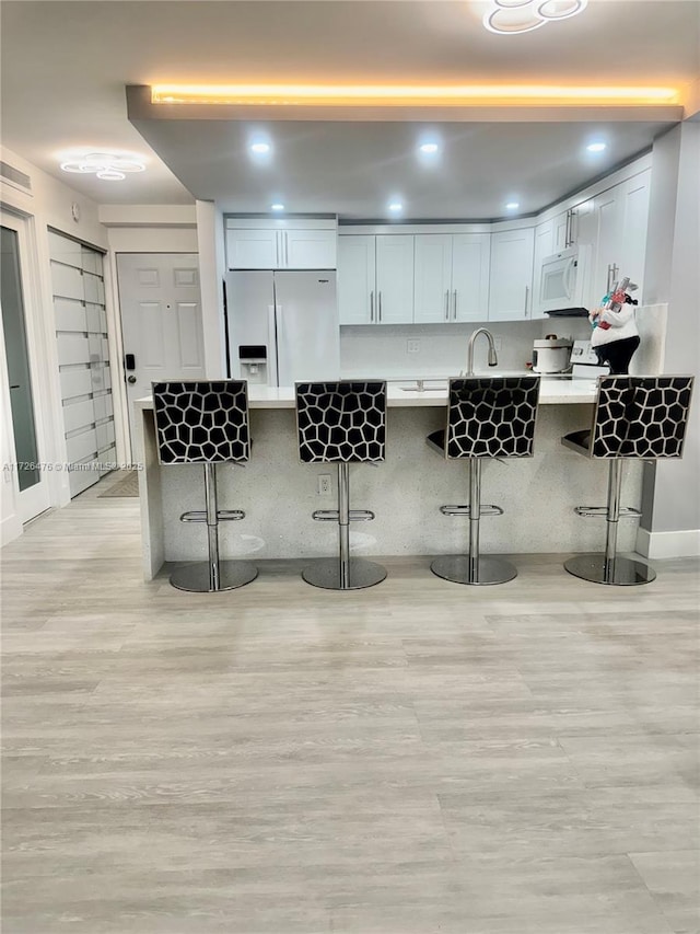 kitchen with white cabinetry, white appliances, a breakfast bar, and kitchen peninsula