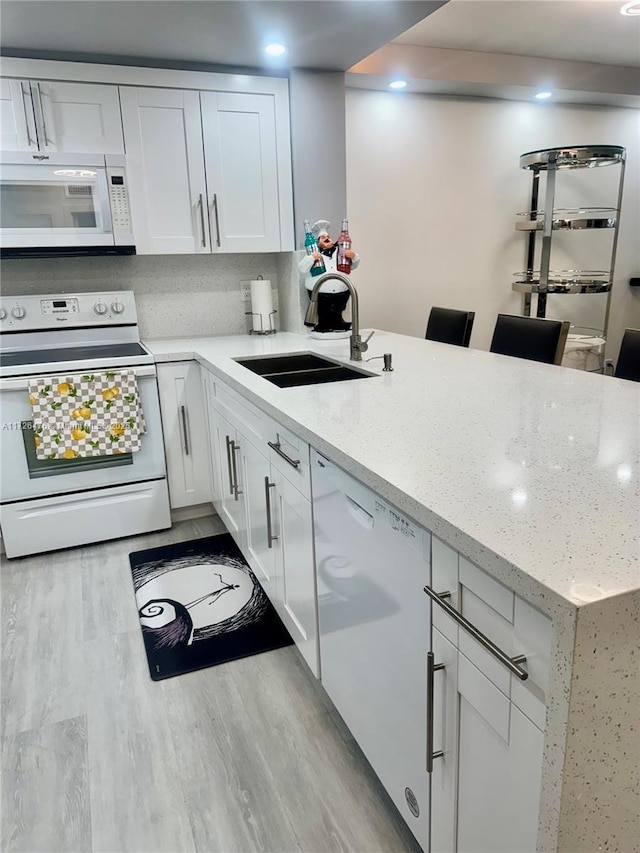 kitchen featuring sink, white cabinets, light stone counters, kitchen peninsula, and white appliances