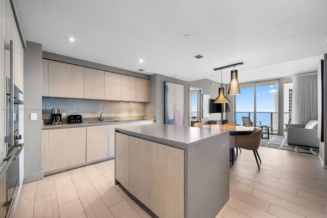 kitchen featuring pendant lighting, a water view, light brown cabinets, and a center island