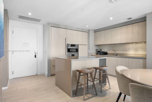 kitchen with stainless steel double oven, a kitchen island, a kitchen bar, light brown cabinets, and decorative backsplash