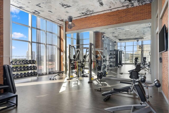 workout area with brick wall, a high ceiling, a wealth of natural light, and a wall of windows