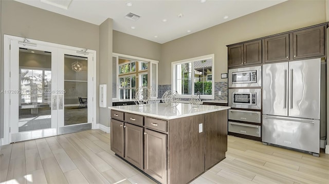 kitchen with light stone counters, dark brown cabinets, a center island, and stainless steel appliances