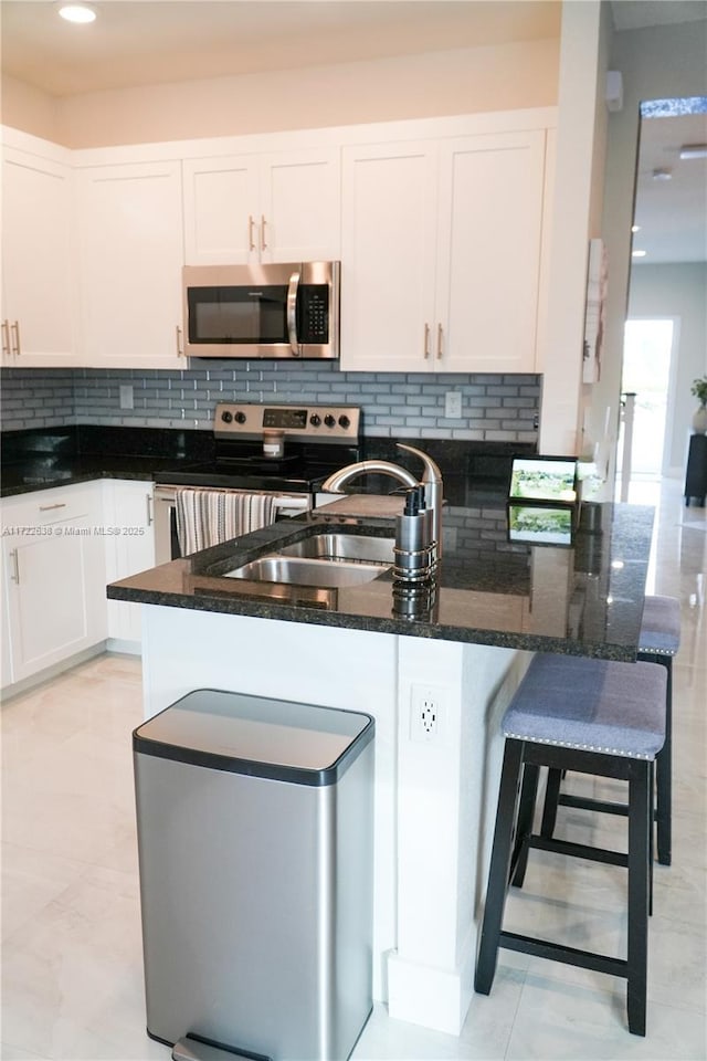 kitchen with white cabinetry, stainless steel appliances, decorative backsplash, dark stone counters, and sink