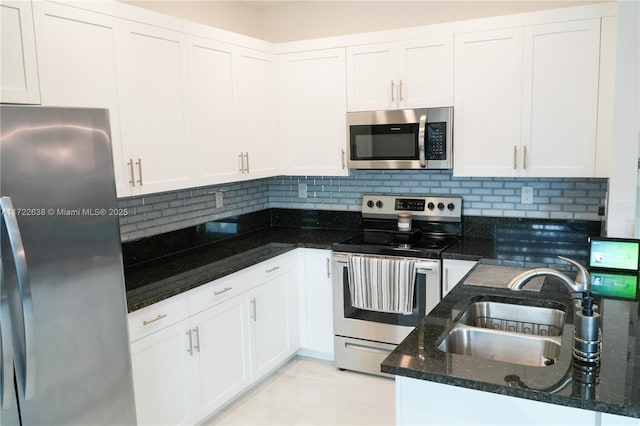 kitchen featuring white cabinets, appliances with stainless steel finishes, dark stone counters, decorative backsplash, and sink