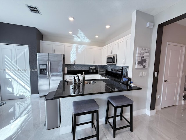 kitchen with white cabinets, appliances with stainless steel finishes, dark stone counters, sink, and a breakfast bar area