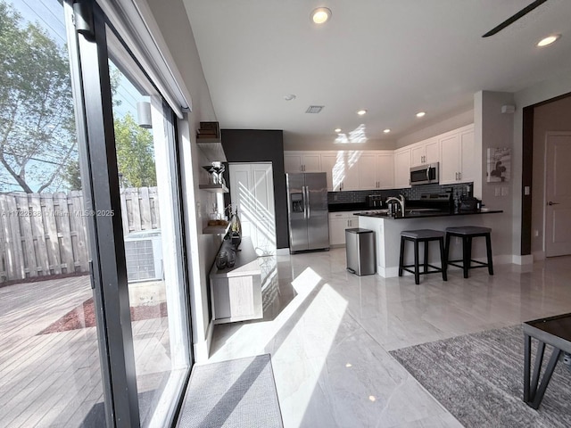 kitchen featuring a kitchen bar, a center island with sink, appliances with stainless steel finishes, backsplash, and white cabinets