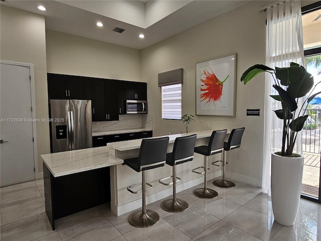 kitchen with a kitchen island, a high ceiling, appliances with stainless steel finishes, a breakfast bar area, and light tile patterned floors