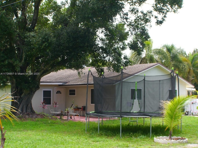 back of property featuring a yard, a patio, and a trampoline