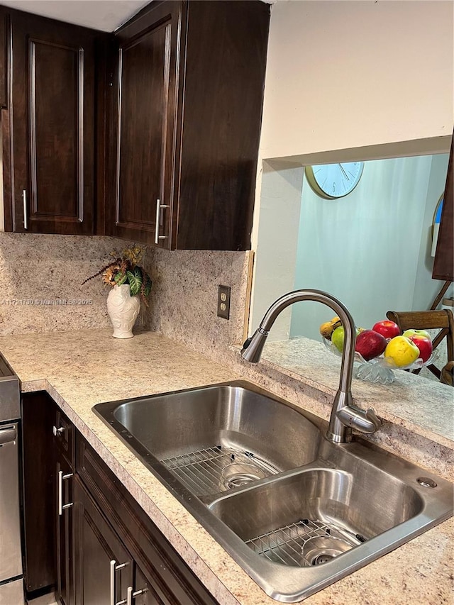 kitchen featuring sink, backsplash, dark brown cabinets, and stove