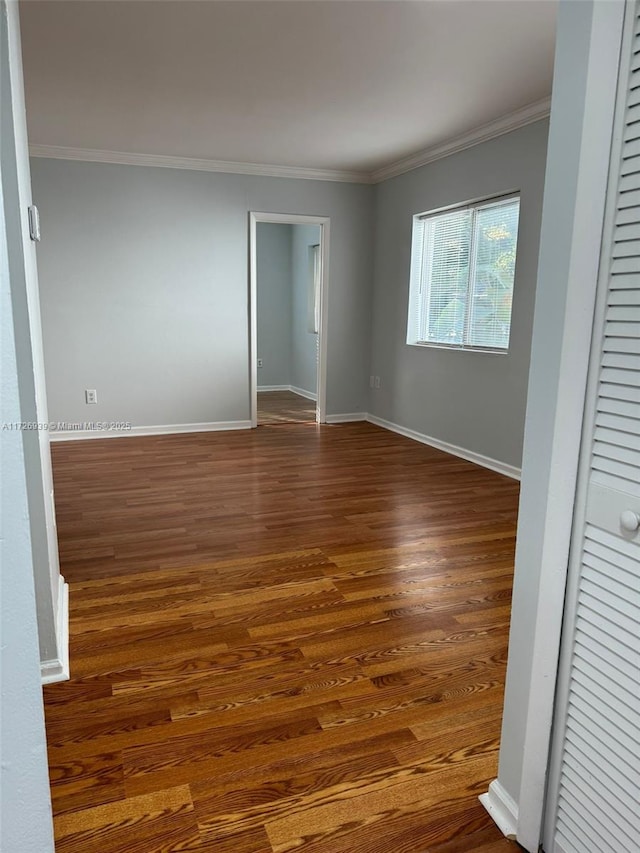 unfurnished room featuring crown molding, dark wood-style floors, and baseboards