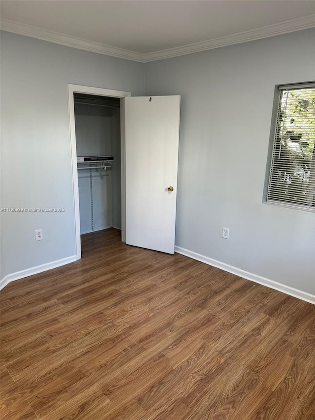 unfurnished bedroom with a closet, baseboards, dark wood-style floors, and ornamental molding