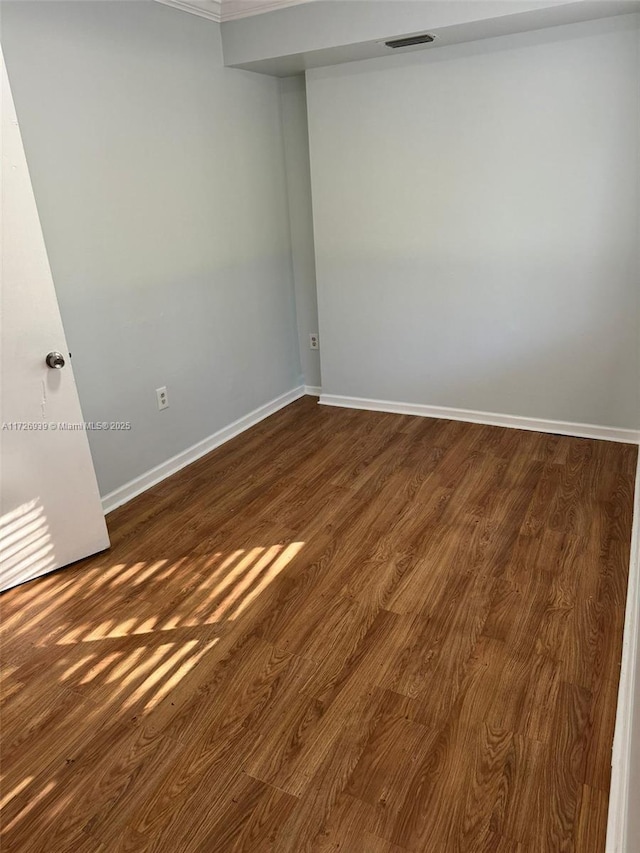 empty room featuring dark wood-style floors, visible vents, and baseboards