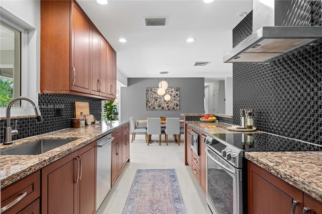 kitchen with pendant lighting, appliances with stainless steel finishes, wall chimney exhaust hood, sink, and light stone counters