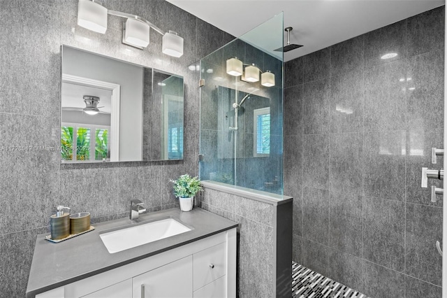 bathroom featuring ceiling fan, vanity, tile walls, and tiled shower