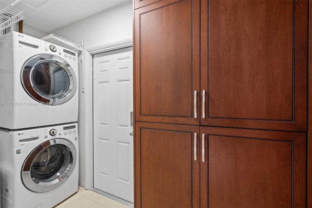 clothes washing area featuring light tile patterned floors, stacked washer and dryer, and cabinets