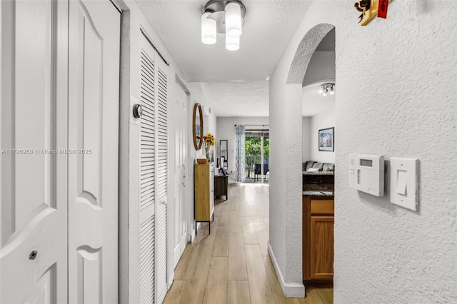 corridor with a textured ceiling and light hardwood / wood-style flooring