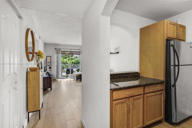 kitchen featuring light hardwood / wood-style floors, a textured ceiling, stainless steel fridge, and dark stone counters