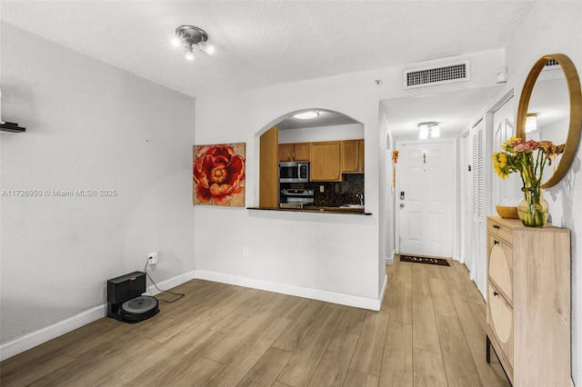 kitchen featuring a textured ceiling, stainless steel appliances, decorative backsplash, and light hardwood / wood-style flooring