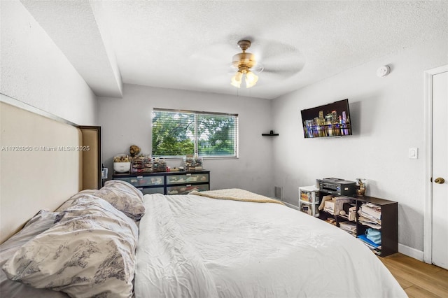 bedroom with a textured ceiling, ceiling fan, and hardwood / wood-style floors