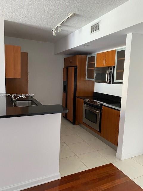 kitchen with light tile patterned floors, sink, stainless steel appliances, and a textured ceiling