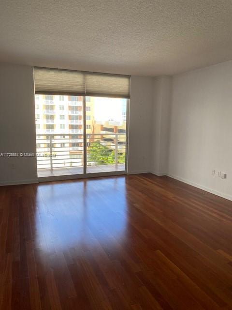 empty room featuring a wealth of natural light, dark hardwood / wood-style floors, expansive windows, and a textured ceiling