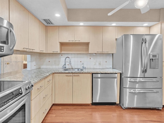 kitchen with appliances with stainless steel finishes, light brown cabinetry, backsplash, and sink