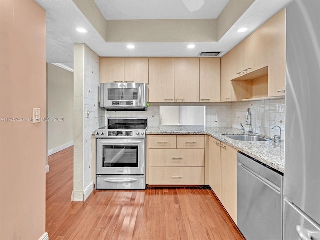 kitchen featuring light stone countertops, stainless steel appliances, light brown cabinetry, sink, and light hardwood / wood-style flooring