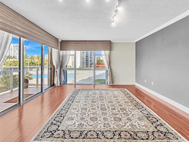 interior space with a textured ceiling, ornamental molding, track lighting, and hardwood / wood-style floors