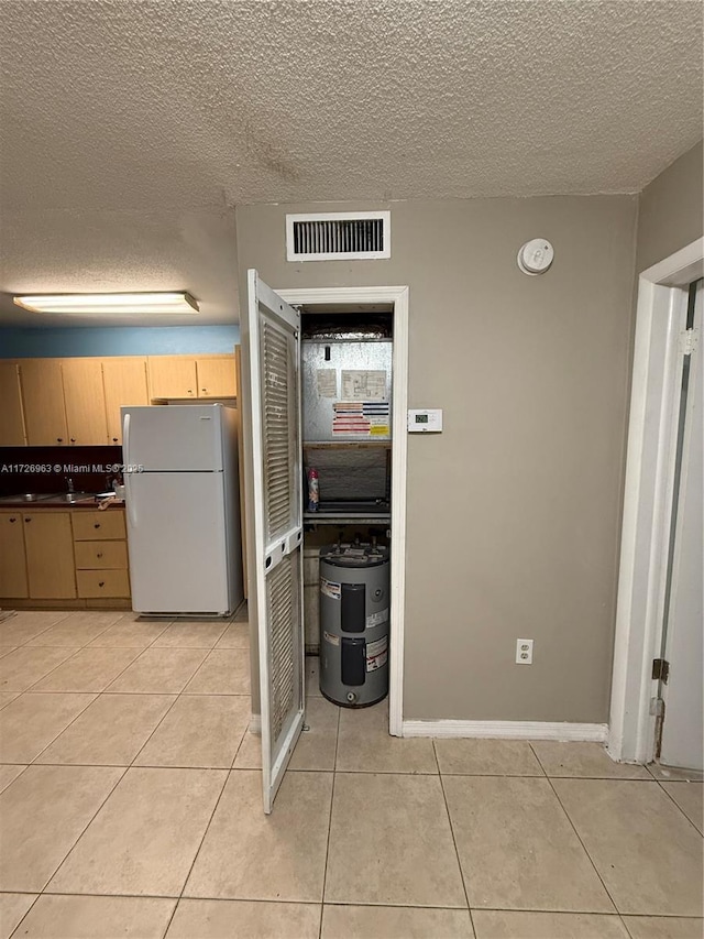 kitchen with light tile patterned floors, light brown cabinetry, white refrigerator, and a textured ceiling