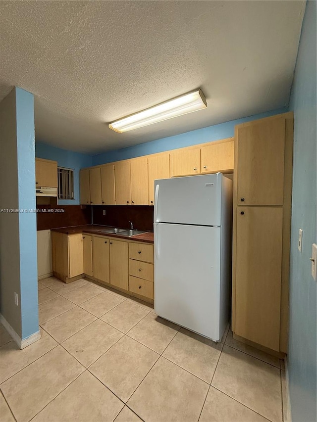 kitchen with light tile patterned floors, light brown cabinets, a textured ceiling, white refrigerator, and sink