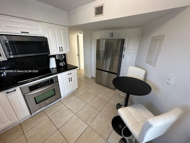 kitchen with tasteful backsplash, light tile patterned floors, stainless steel appliances, a textured ceiling, and white cabinets