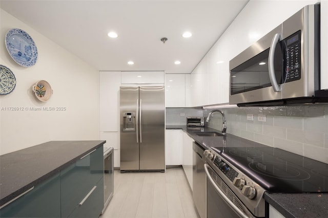 kitchen featuring white cabinets, modern cabinets, appliances with stainless steel finishes, dark stone countertops, and a sink