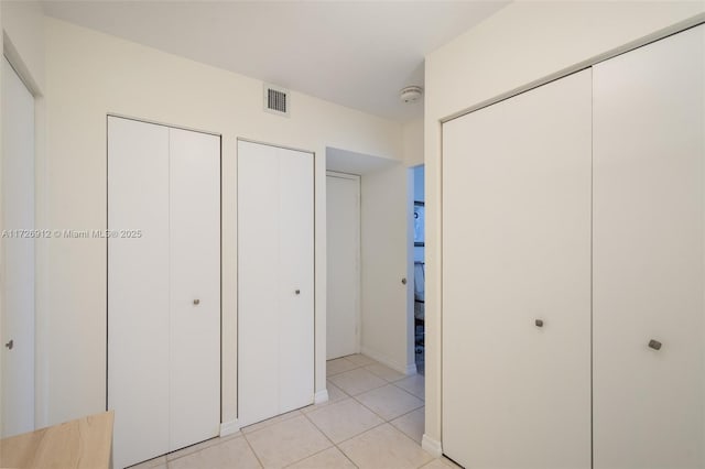 unfurnished bedroom with light tile patterned floors, visible vents, and two closets