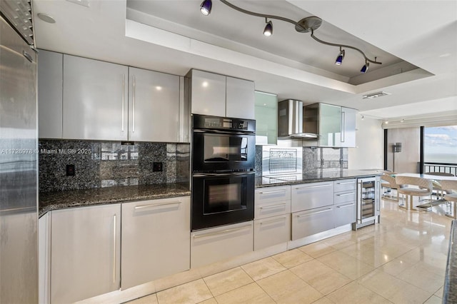 kitchen featuring white cabinetry, wall chimney range hood, double oven, wine cooler, and a tray ceiling