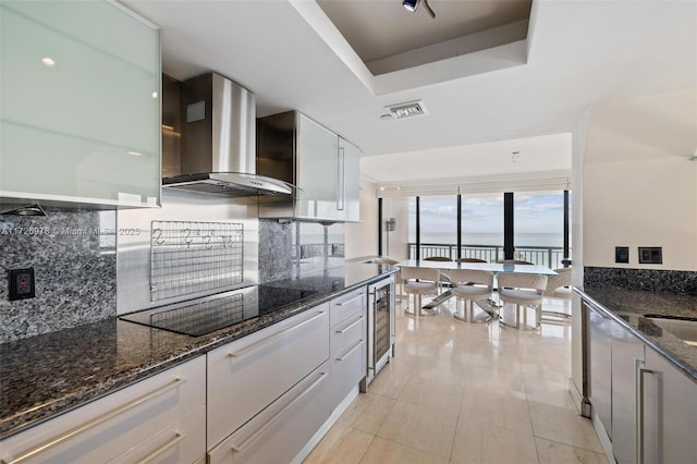 kitchen featuring white cabinetry, wall chimney range hood, dark stone countertops, a tray ceiling, and black electric cooktop