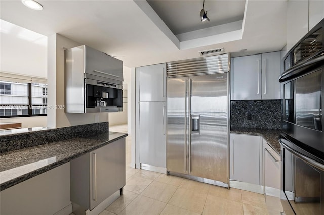 kitchen with double oven, stainless steel built in fridge, dark stone countertops, and rail lighting