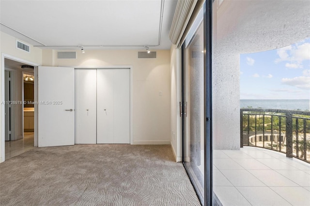 unfurnished bedroom with a closet, track lighting, a water view, and light colored carpet