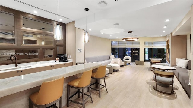 bar featuring pendant lighting, light hardwood / wood-style flooring, light stone counters, and sink