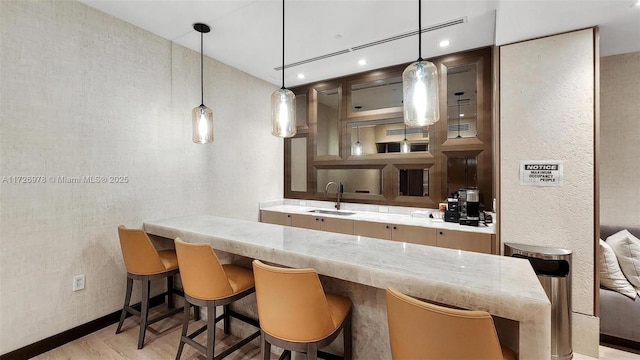 kitchen with sink, hanging light fixtures, a breakfast bar area, and light wood-type flooring